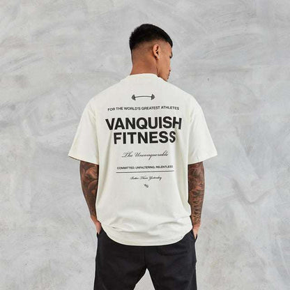 Man wearing white Fitness Boxy Oversized T-Shirt with black text on back, paired with black pants, against gray background