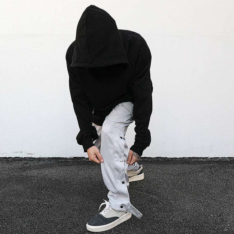 Person wearing black hoodie adjusting grey ankle snap cargo pants with snap buttons along the sides